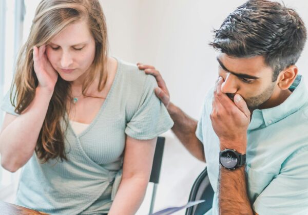 A young couple sits with a real estate agent, reviewing documents and looking concerned about buying a new home.